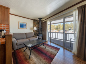 One bedroom lakeside condo living room with sofa, coffee table, wood fireplace and balcony