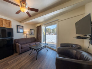 Two bedroom condo at Tahoe Sands Resort living room with sofa, two armchairs, coffee table, ceiling fan, black refrigerator.