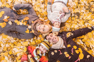 family of four laying on yellow autumn leaves smiling for photo